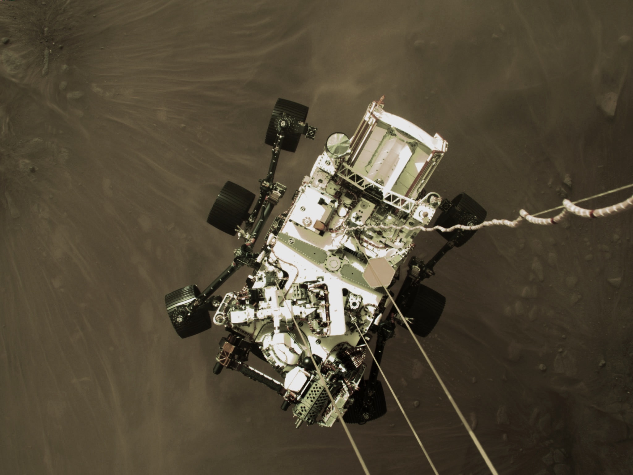 Foto en la que se puede ver la etapa de descenso que sostiene el rover Perseverance de la NASA cayendo a través de la atmósfera marciana, con su paracaídas detrás.